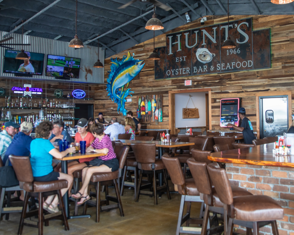 National Oyster Day Shines Bright with the Golden Oyster at Hunt’s in Panama City: A Truly Unforgettable Celebration 4 Guests enjoy seafood inside Hunt's Oyster Bar in Panama City, Florida during National Oyster Day, with a rustic wooden interior and local artwork.