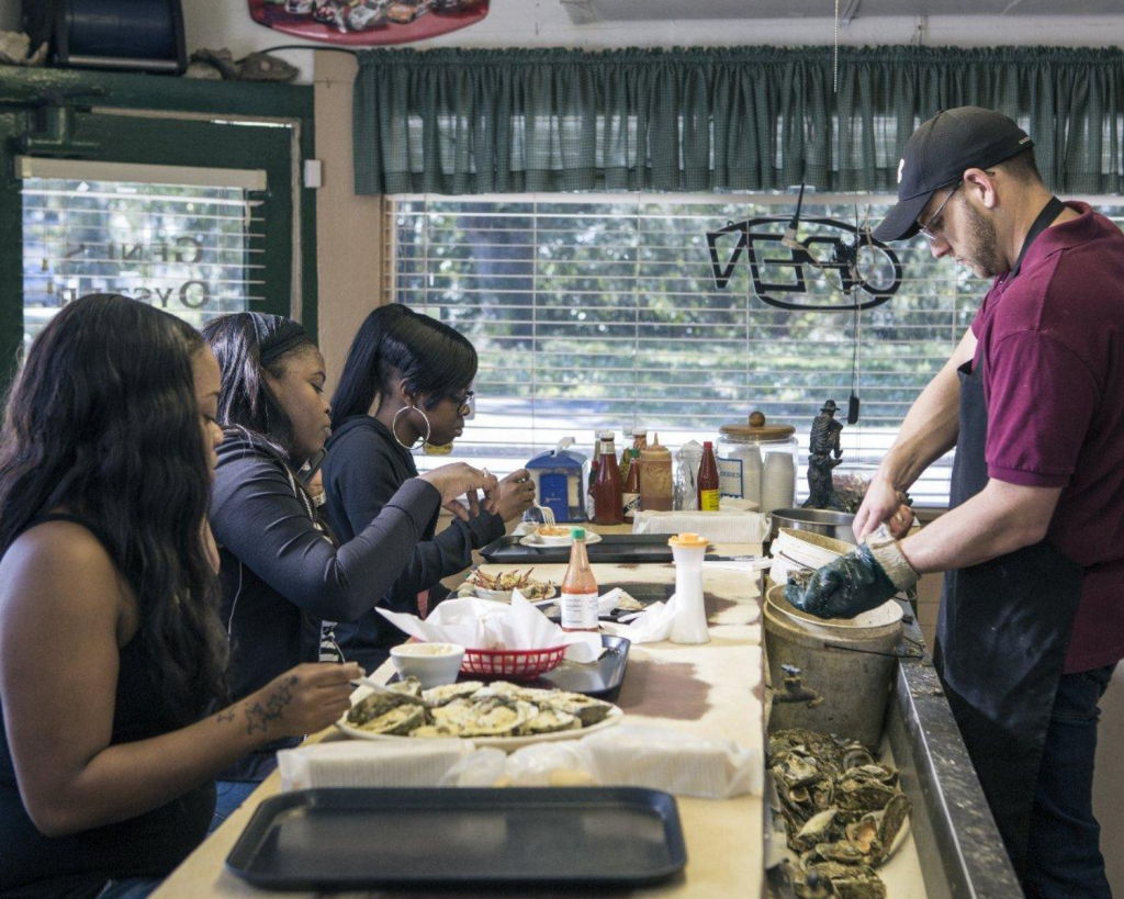 Guests enjoy fresh seafood at the counter while oysters are shucked in front of them at Gene's Oyster Bar in Panama City, Florida.


