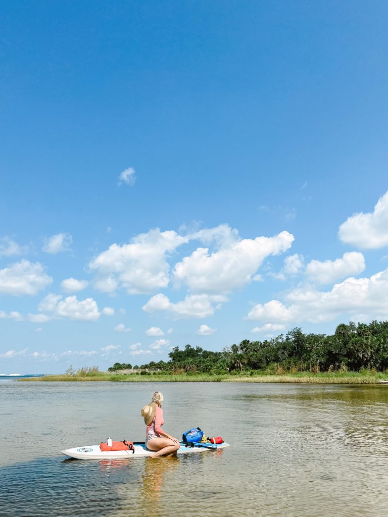 A girl sitting on a paddleboard in the calm waters of St. Andrews Bay, enjoying a relaxing spot in Panama City.