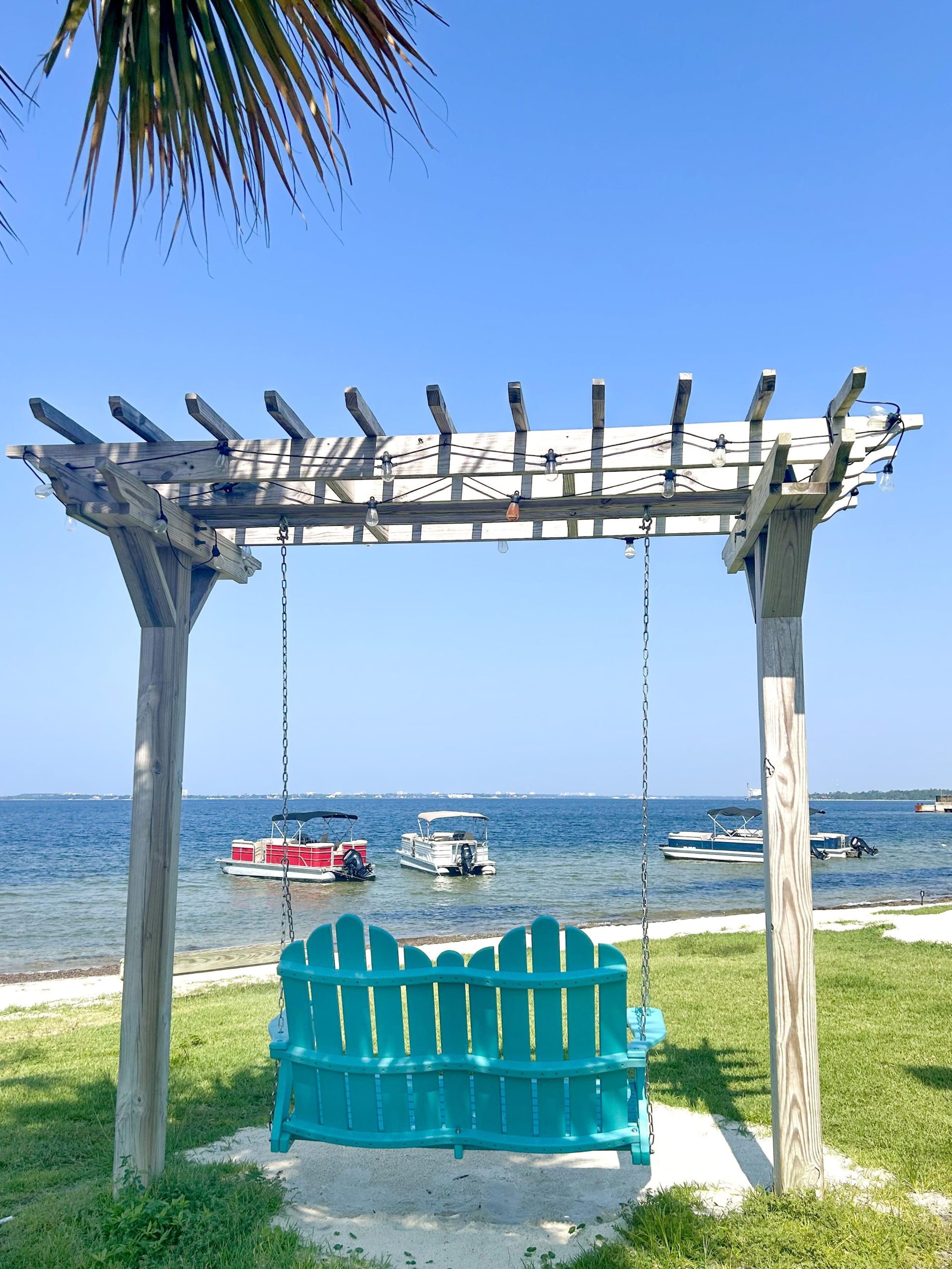 A blue Adirondack swing on the Destination Panama City lawn overlooking St. Andrews Bay, a perfect relaxing spot in Panama City.