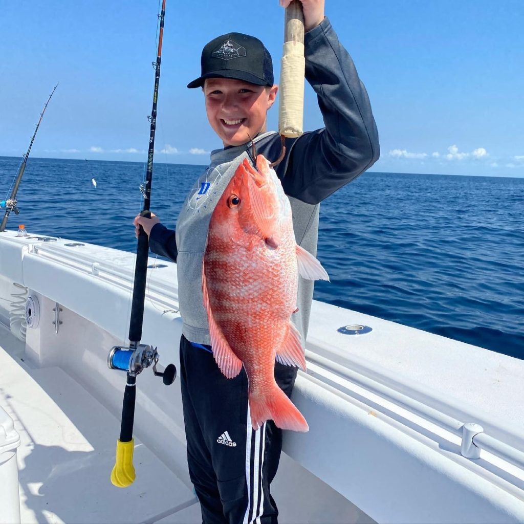 A boy smiling on a boat while holding up his fresh catch on a fishing pole, capturing the excitement of sea-to-table dining and Florida eco-adventures during sustainable travel in Panama City.