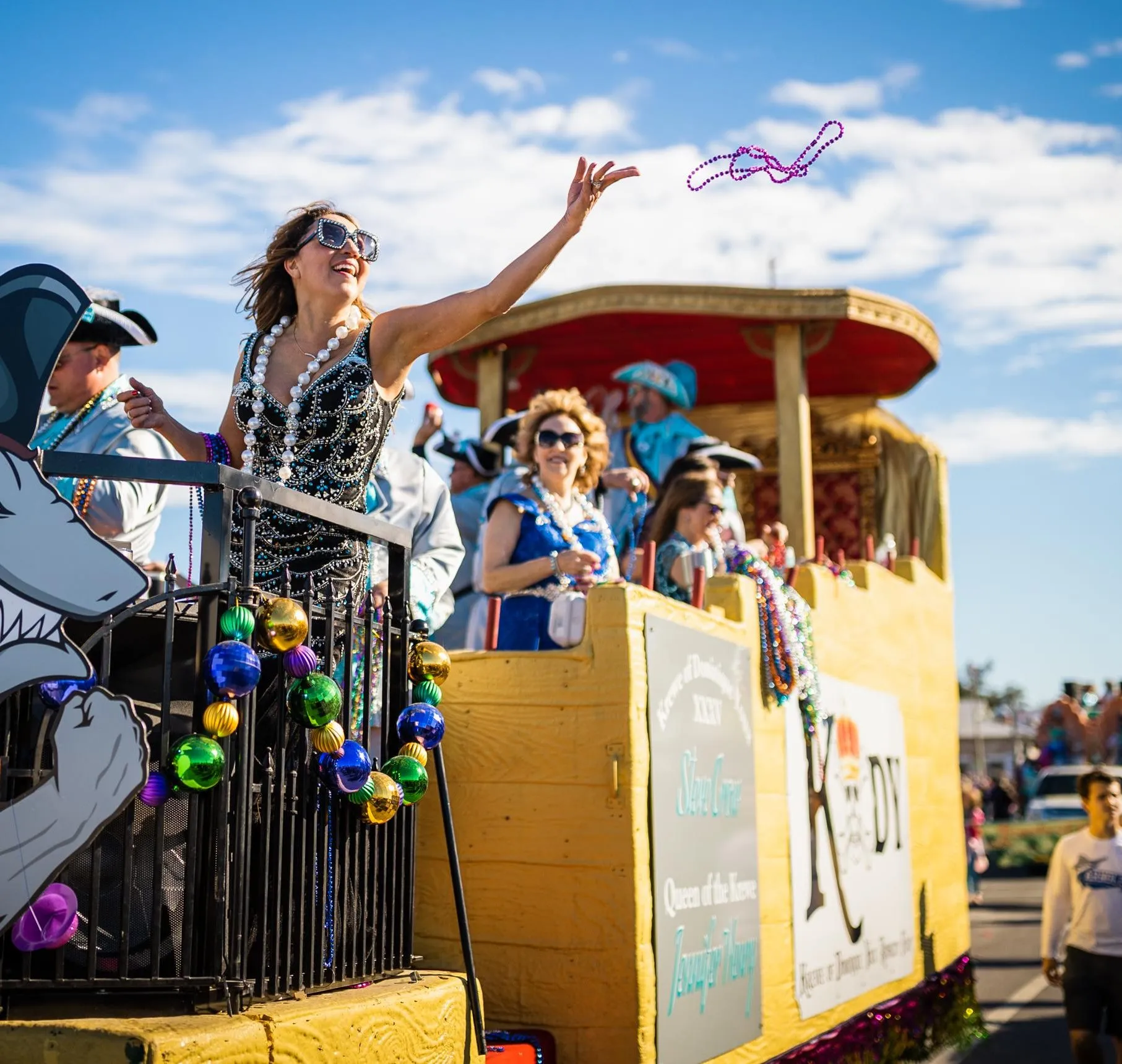 Mardi Gras celebration in Historic St. Andrews during winter in Panama City, with a woman tossing purple beads from a yellow parade float