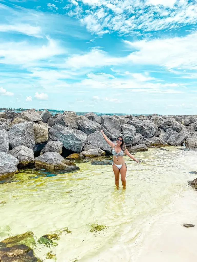 3 Fun Spots for Snorkeling in Panama City, Florida: Where to Go and What to Know 12 Woman standing in clear shallow water near rock jetties, a popular spot for snorkeling in Panama City, Florida.