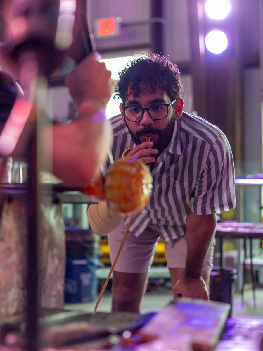 Guest blowing into a glassblowing rod at Panama City Hot Glass, a one of a kind skillcation experience in Florida