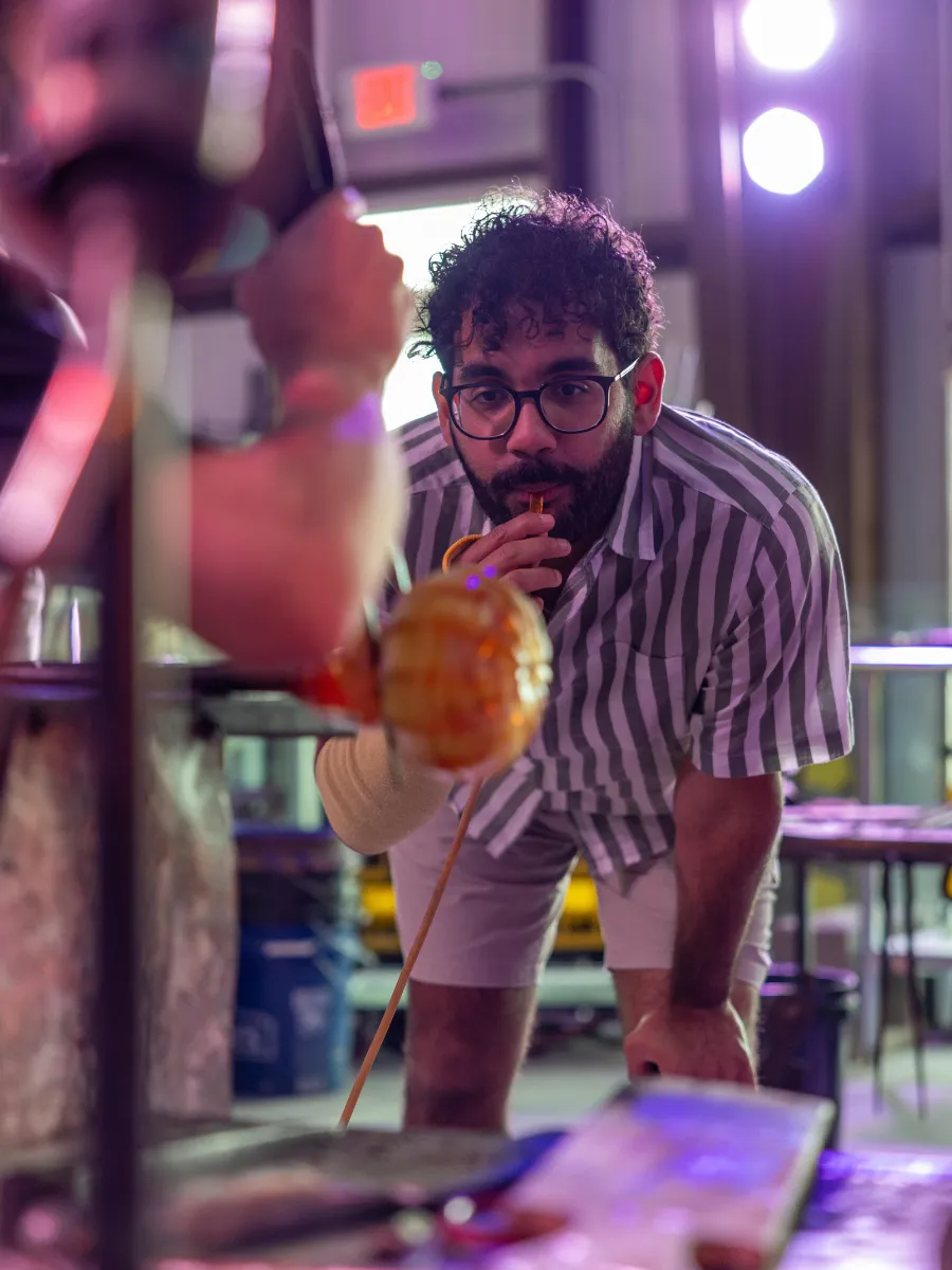 Guest blowing into a glassblowing rod at Panama City Hot Glass, a one of a kind skillcation experience in Florida