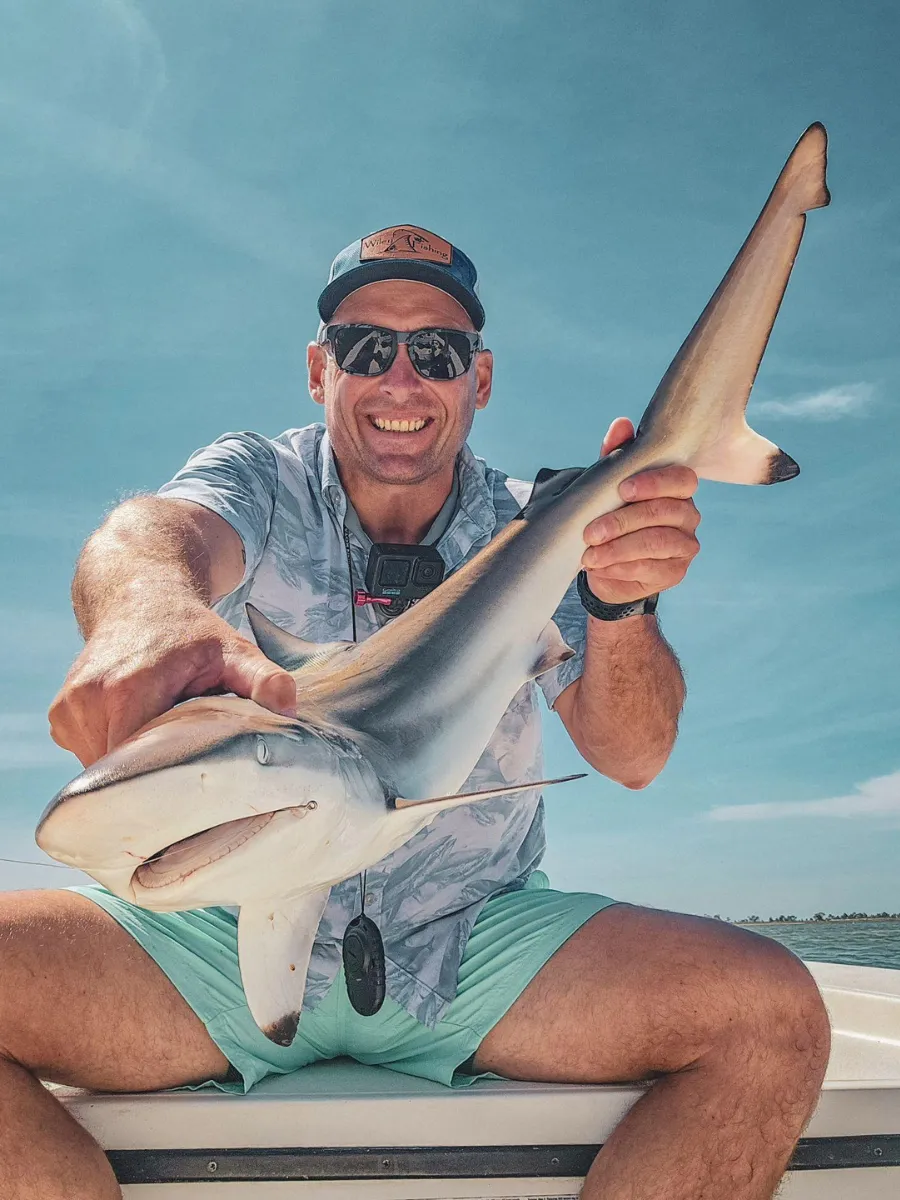 Angler holding a shark caught inshore near Panama City, showcasing the variety of types of fishing in Panama City FL