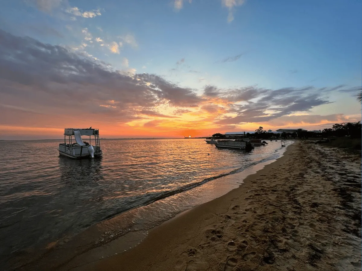 Pontoon boats resting along a bayside beach at sunset in Panama City Florida.