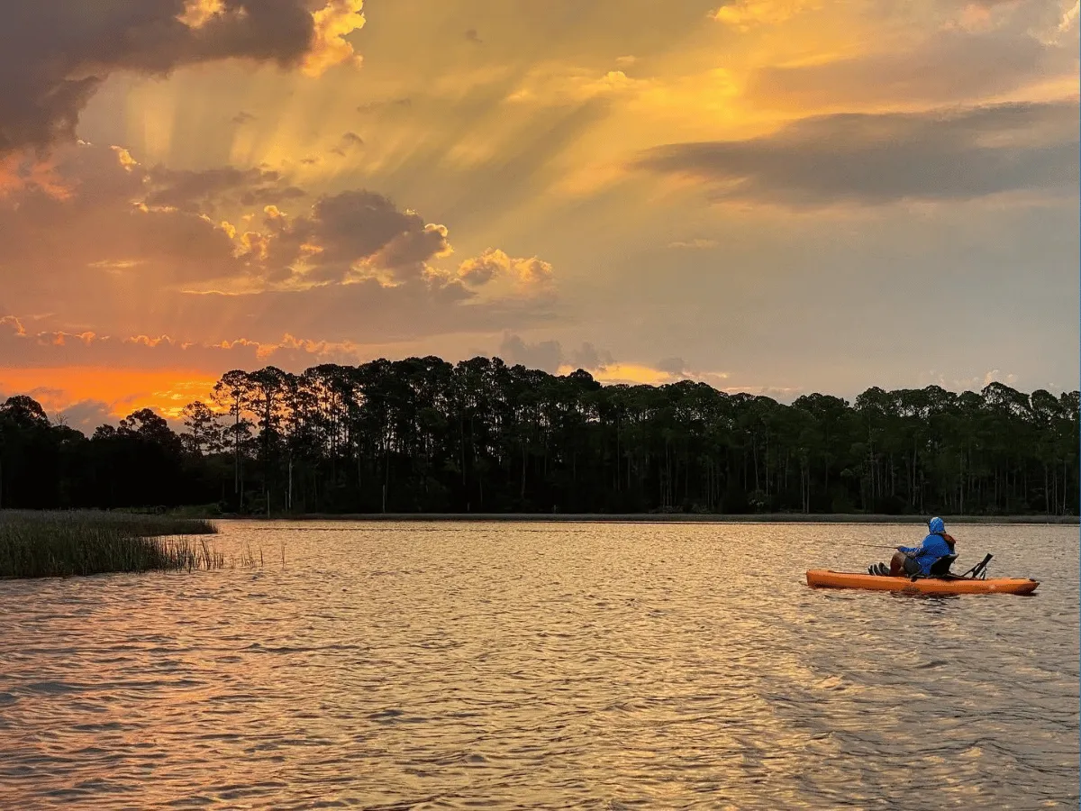 Angler kayaking beneath golden evening skies during sunset in Panama City Florida.