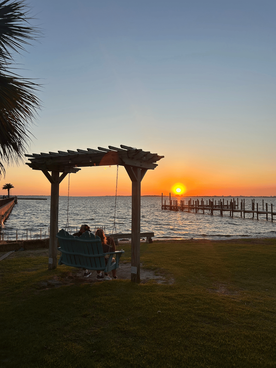 Where to Watch the Best Sunset in Panama City, Florida 8 Visitors relaxing on a waterfront swing during sunset in Panama City Florida.