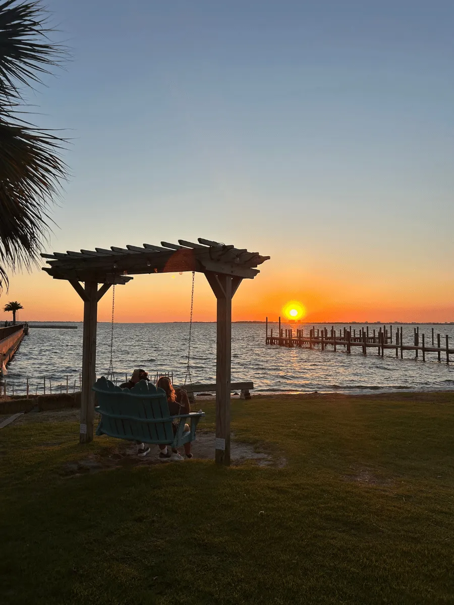 Visitors relaxing on a waterfront swing during sunset in Panama City Florida.