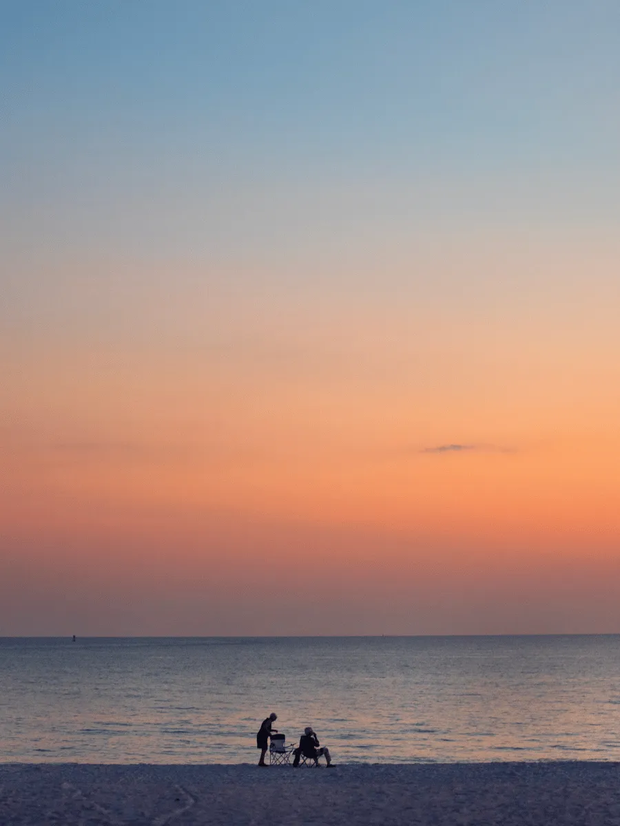 Visitors relaxing on the beach at St. Andrews State Park beneath a soft orange sunset in Panama City Florida.