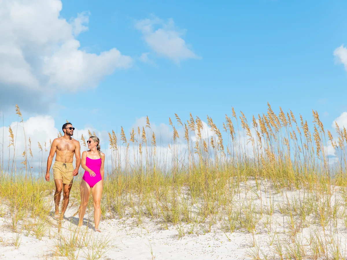 Couple walks along white sand and sea oats while enjoying outdoor things to do in Panama City in the fall.